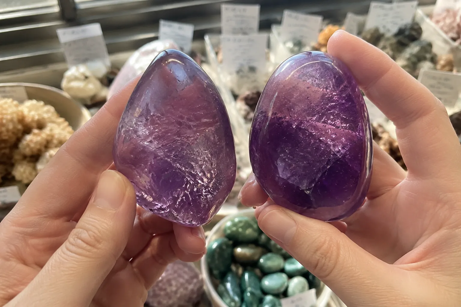A shopper comparing two similar-looking purple polished stones under neutral daylight